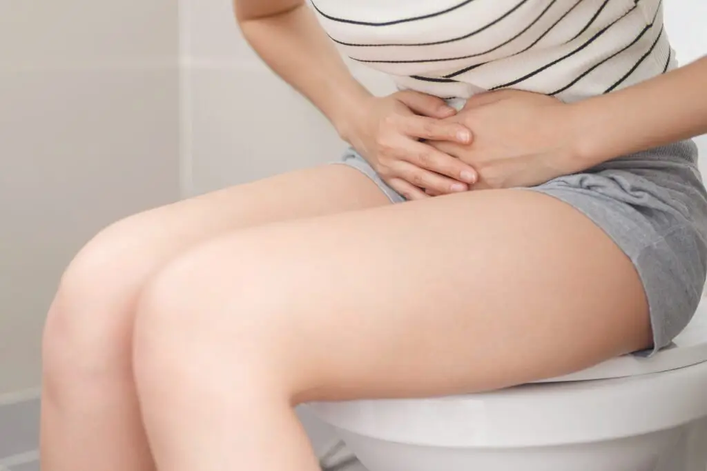 woman sat on the toilet holding her bladder because she is in pain